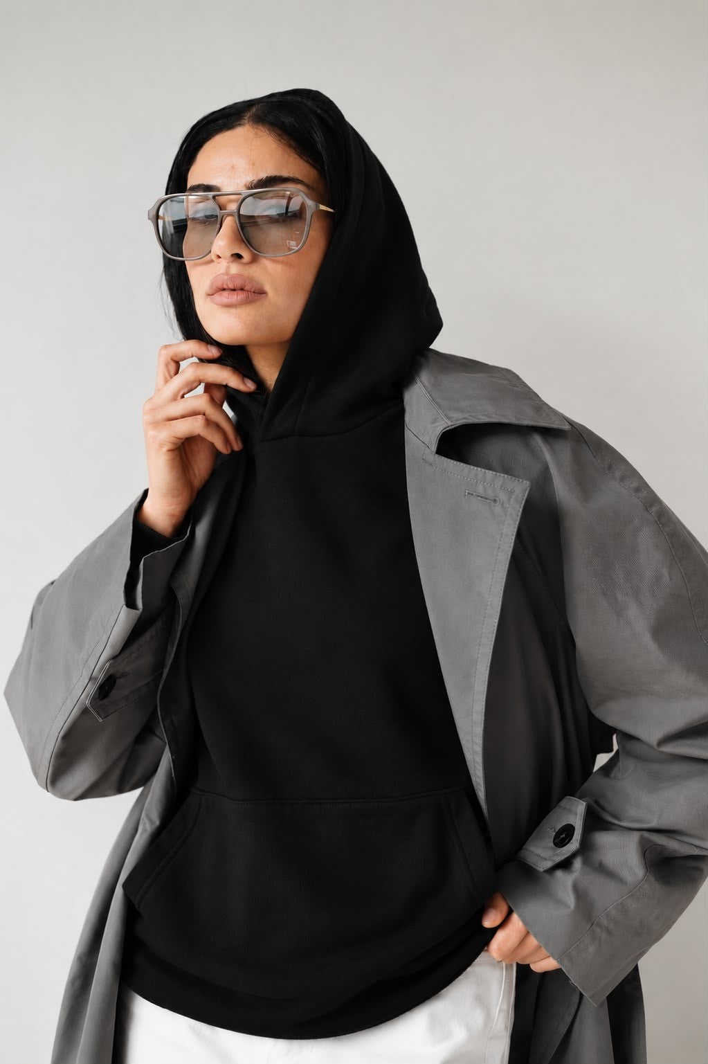 Woman wearing the black Believe hoodie with the hood up under a grey coat