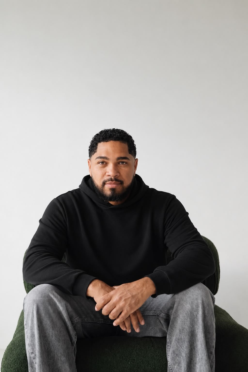 Man seated wearing the black Le Butin8 Believe hoodie with grey trousers