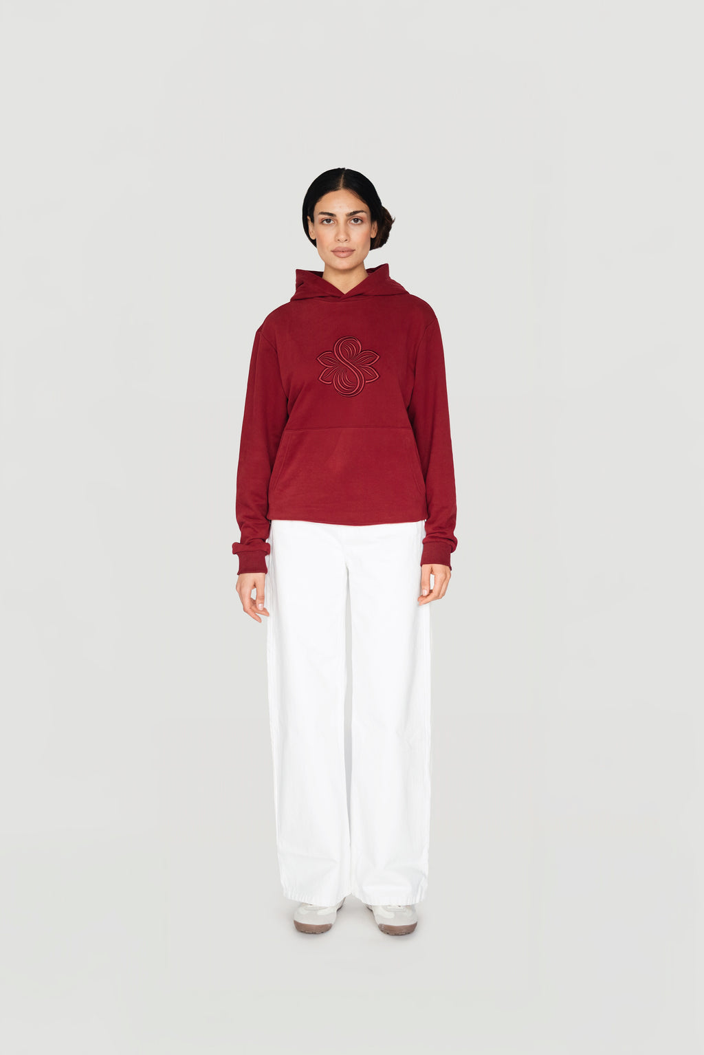 Front view of a woman wearing the bordeaux Le Butin8 Strength hoodie with white trousers