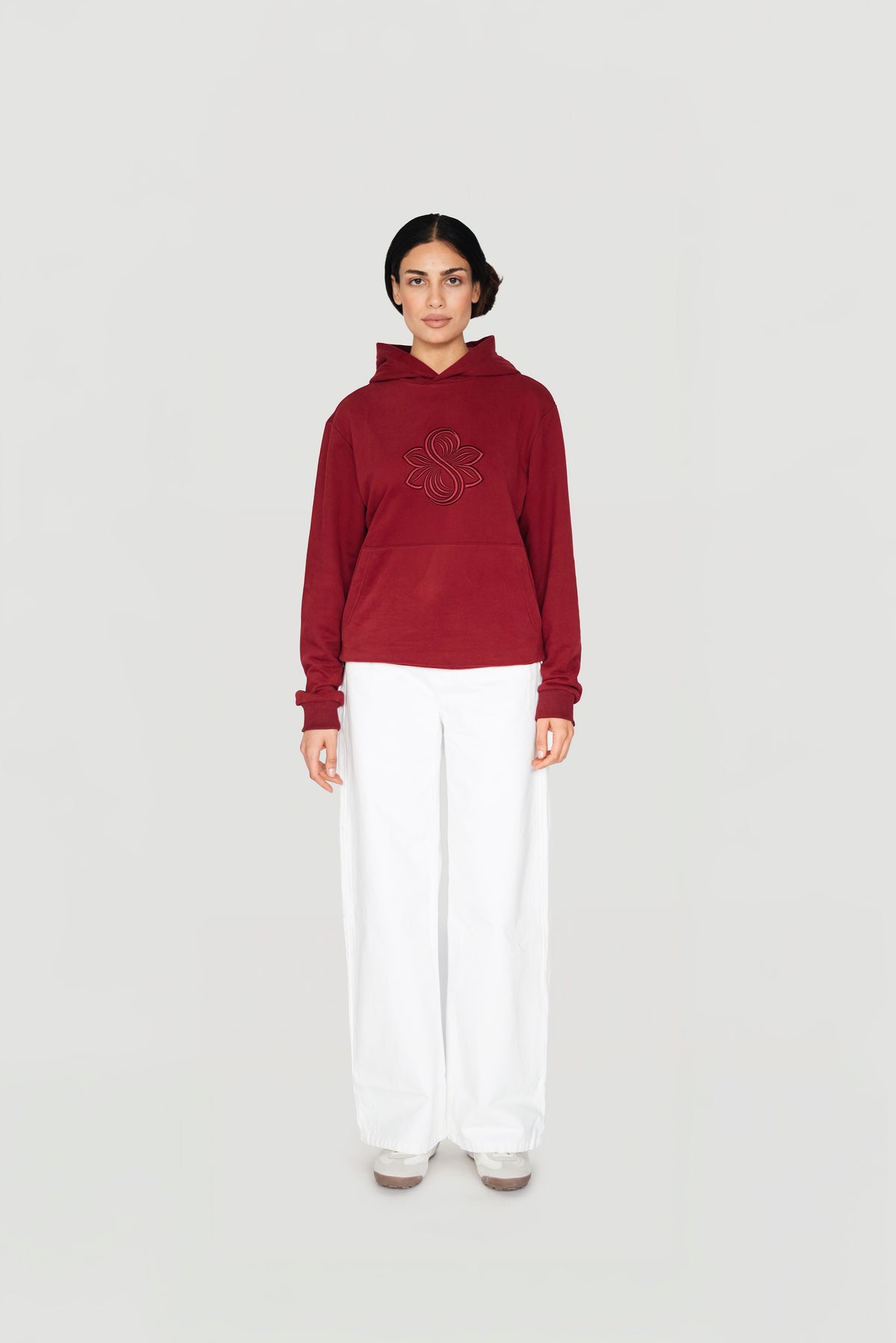 Front view of a woman wearing the bordeaux Le Butin8 Strength hoodie with white trousers