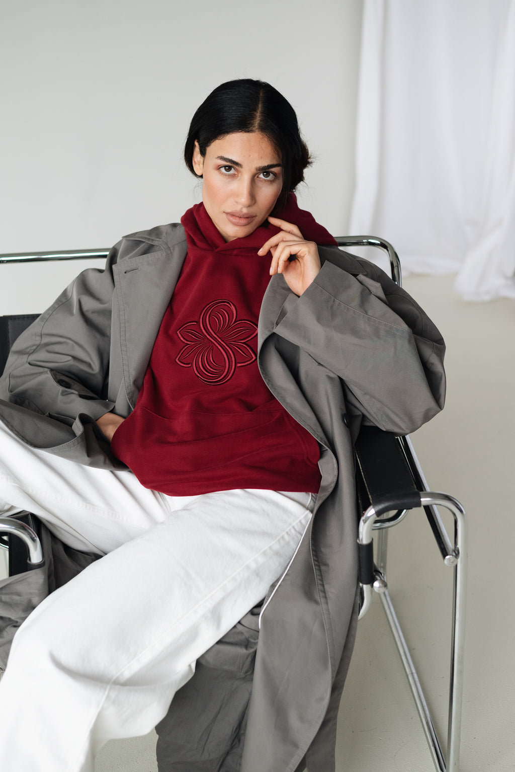 Woman seated wearing the bordeaux Strength hoodie under a grey overcoat