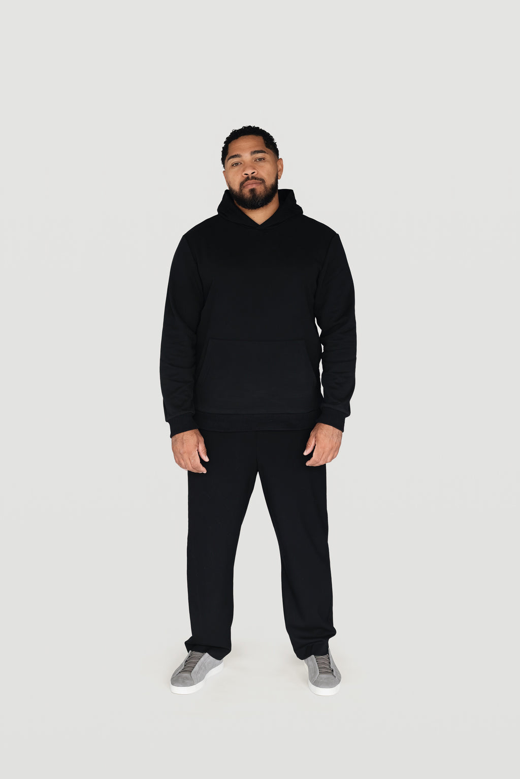 Front view of a man wearing the black Le Butin8 Believe hoodie and matching trousers