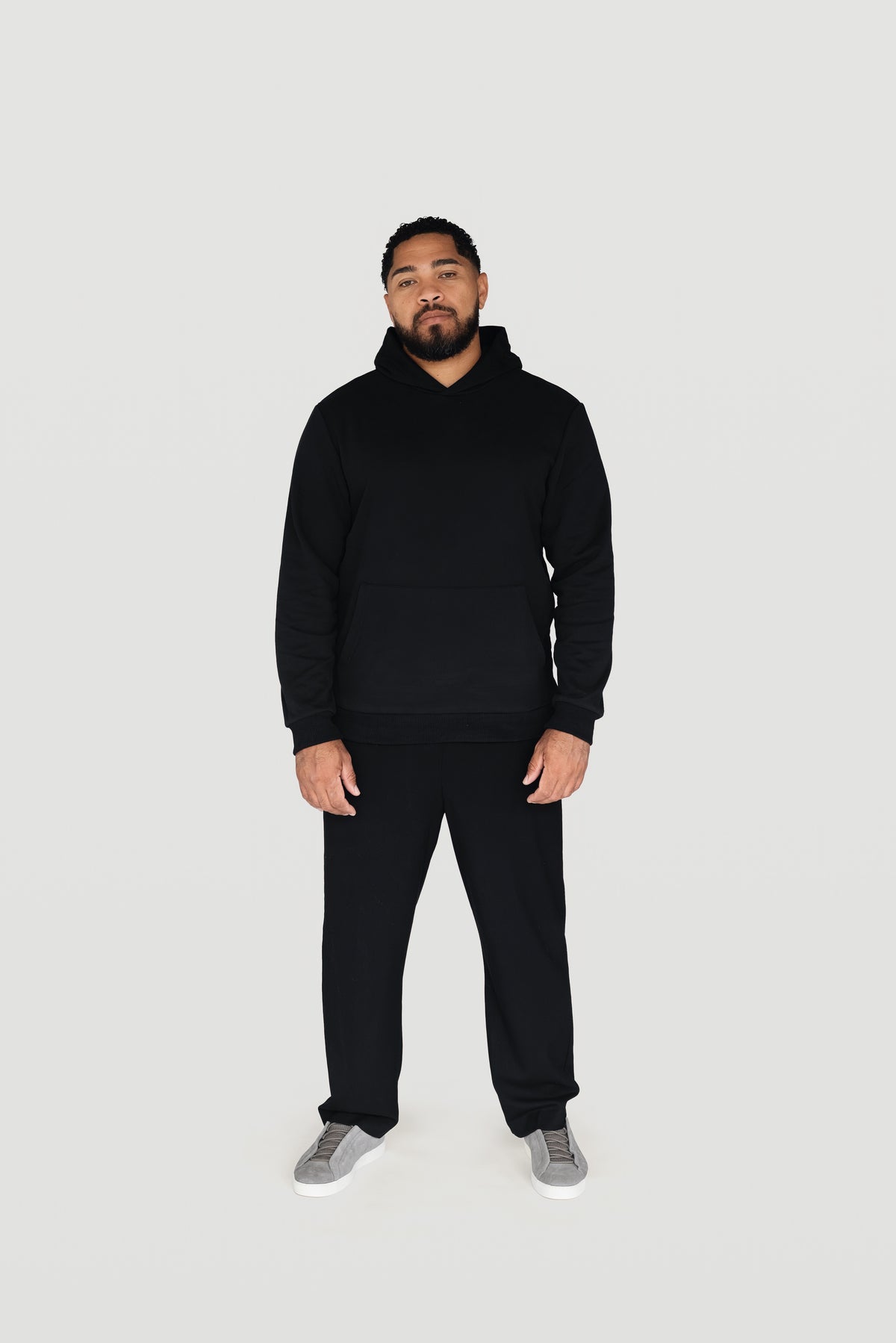 Front view of a man wearing the black Le Butin8 Believe hoodie and matching trousers